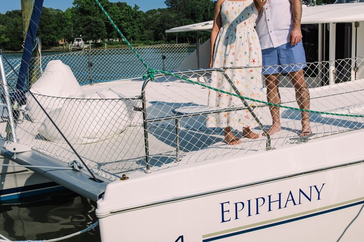 Couple standing on a sailboat named Epiphany, smiling on a sunny day.