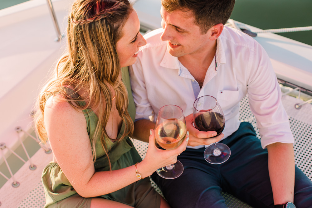 Couple sitting on a boat net holding wine glasses and smiling at each other.