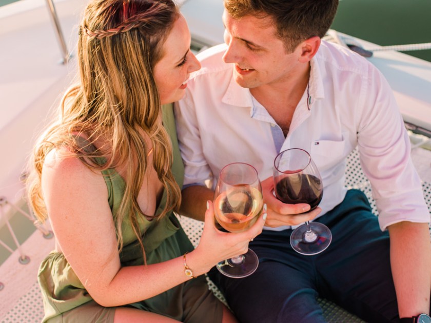 Couple sitting on a boat net holding wine glasses and smiling at each other.