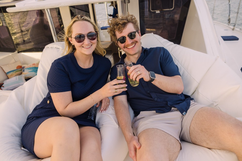 Two people sitting on a boat, toasting drinks and smiling.