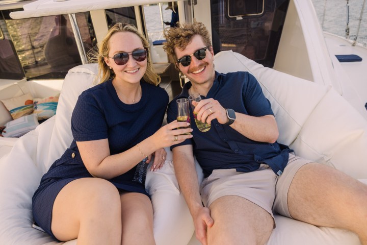 Two people sitting on a boat, toasting drinks and smiling.