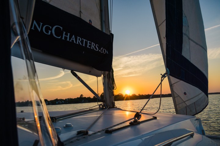 Sailboat on water at sunset with visible sails and calm horizon.