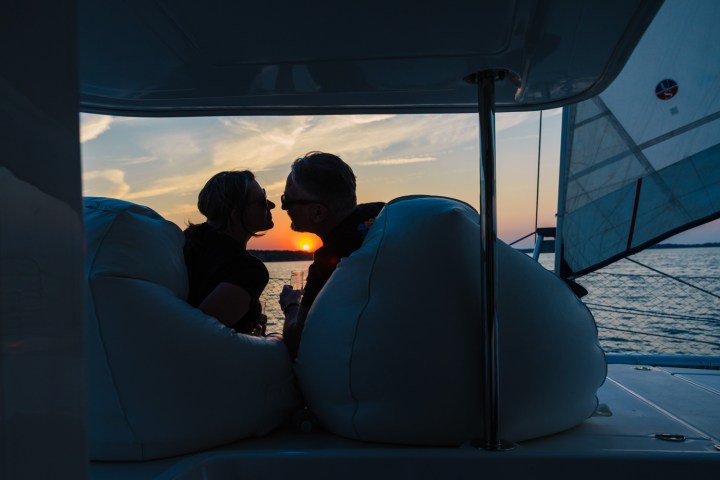 Couple sitting on a boat at sunset, silhouetted against the sky.