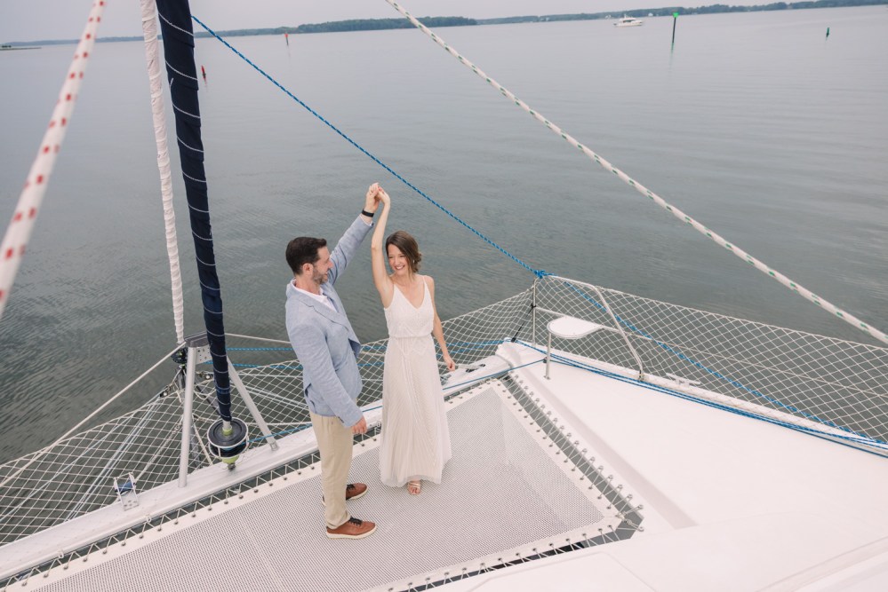 Couple dancing on a sailboat deck over calm water.