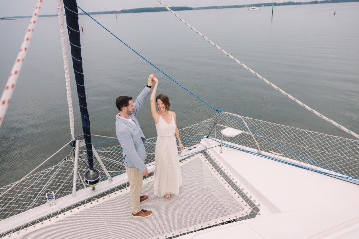 Couple dancing on a sailboat deck over calm water.