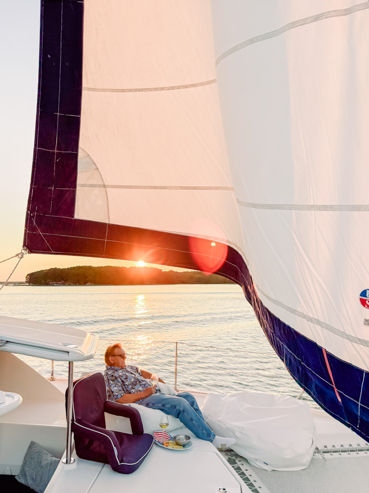 Person relaxing on a sailboat during sunset, with a sail prominently visible.