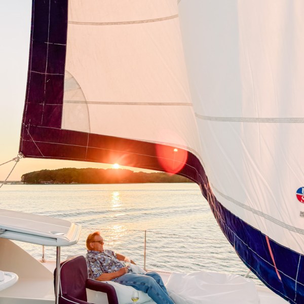 Person relaxing on a sailboat during sunset, with a sail prominently visible.