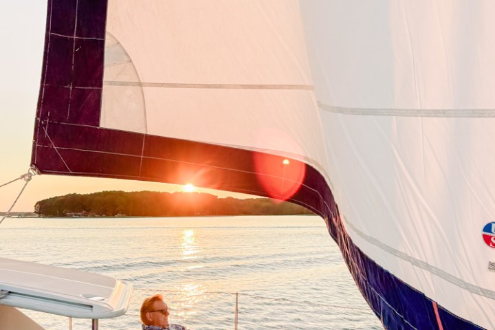 Person relaxing on a sailboat during sunset, with a sail prominently visible.