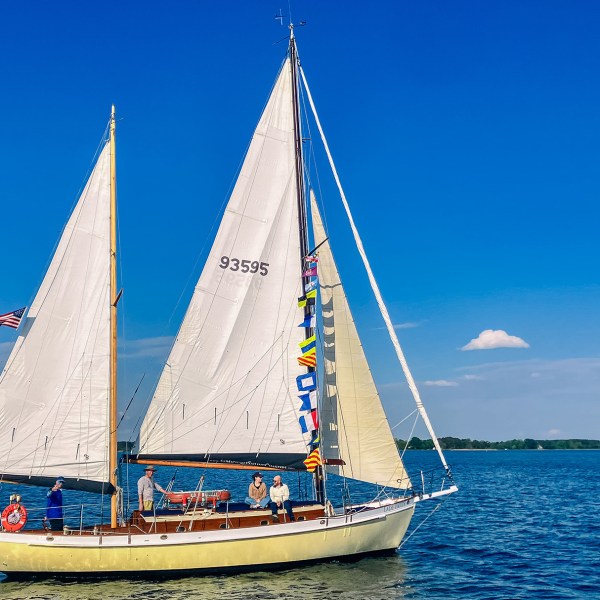 Sailboat with flags on calm water under clear blue sky.