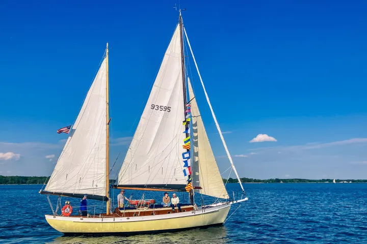 Sailboat with flags on calm water under clear blue sky.