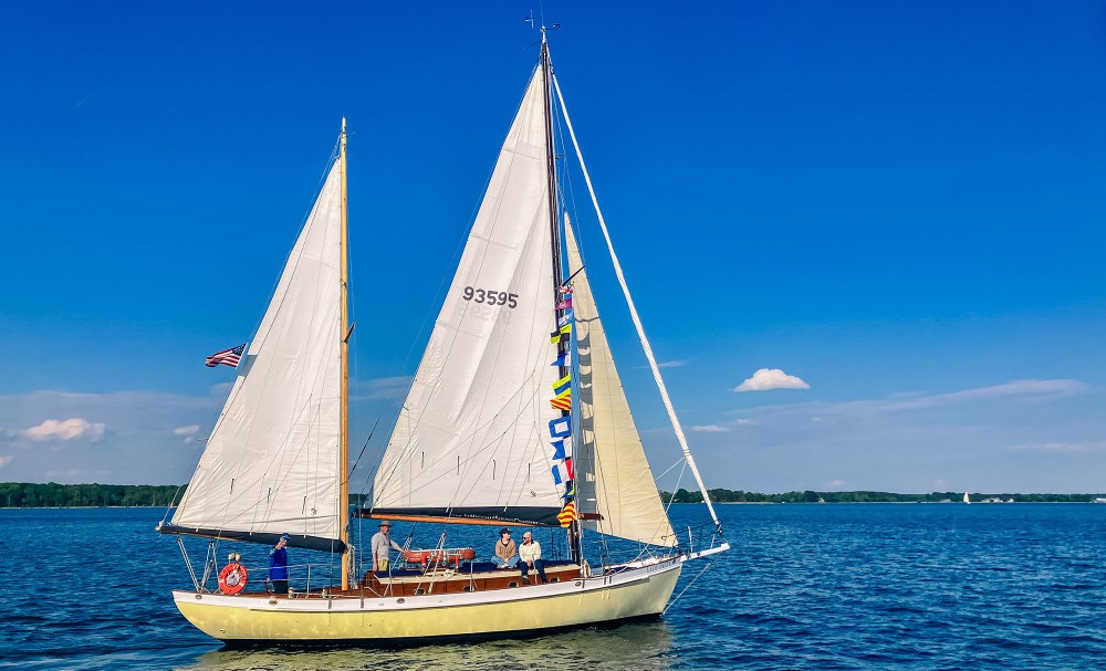 Sailboat with flags on calm water under clear blue sky.