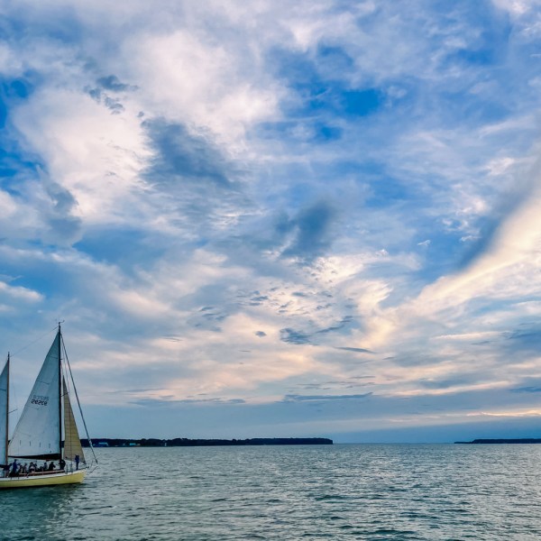 Sailboat on calm water under partly cloudy blue sky.