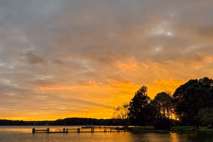 Sunset over calm lake with dock and silhouetted trees.