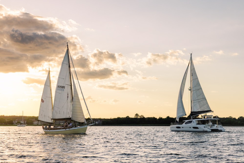 Two sailboats on the water at sunset with clouds in the sky.