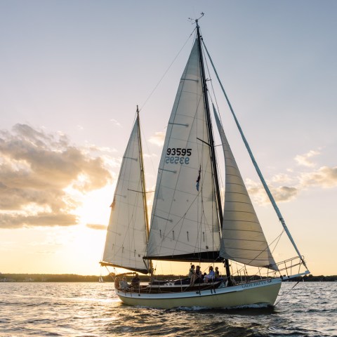 Sailboat with sails up on a lake during sunset, clouds in sky.