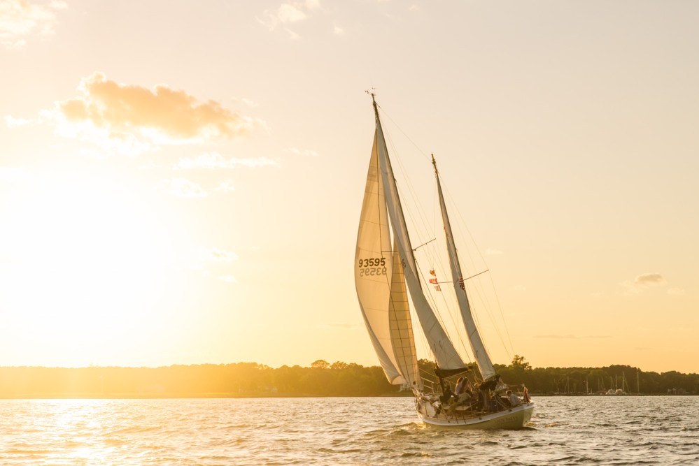 Sailboat on water at sunset with glowing sky and distant shoreline.