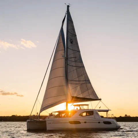 Sailboat on water at sunset with sails up and orange sky.