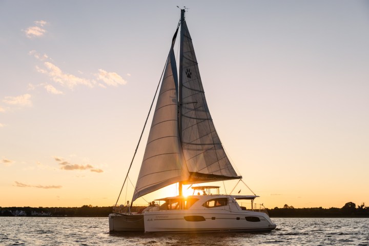 Sailboat on water at sunset with sails up and orange sky.