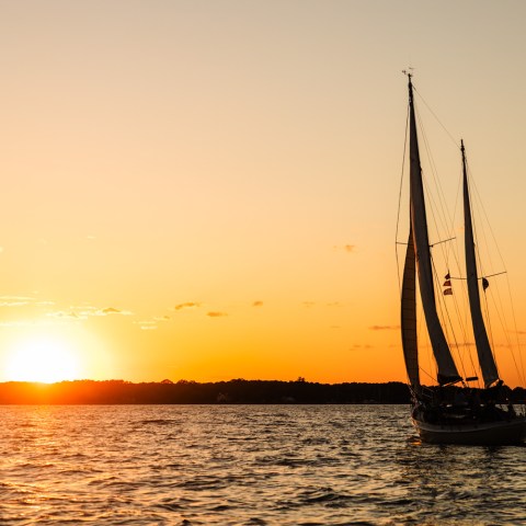 Sailboat on water at sunset with orange sky and horizon.