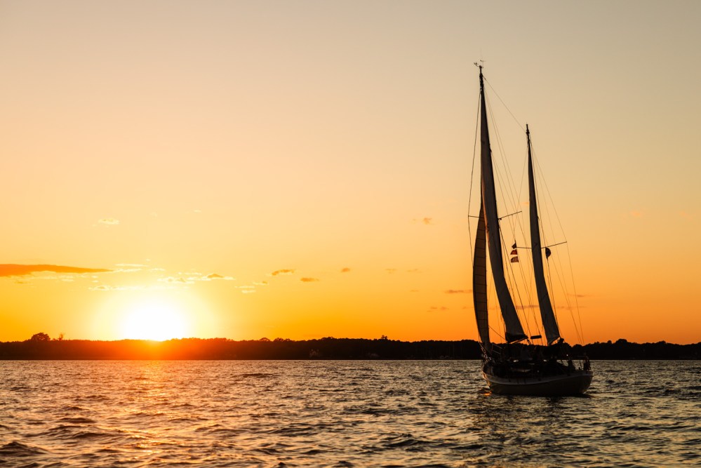 Sailboat on water at sunset with orange sky and horizon.