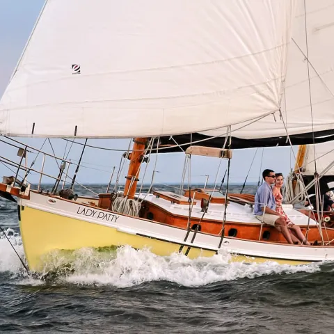 Sailboat 'Lady Patty' on water with three people aboard, sails full in the wind.