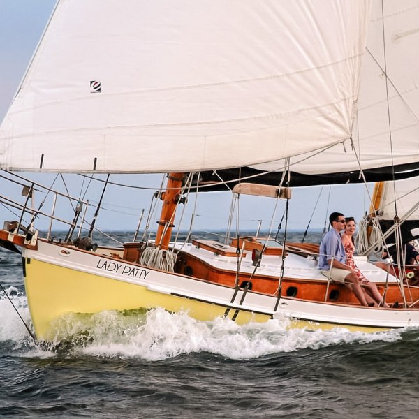 Sailboat 'Lady Patty' on water with three people aboard, sails full in the wind.