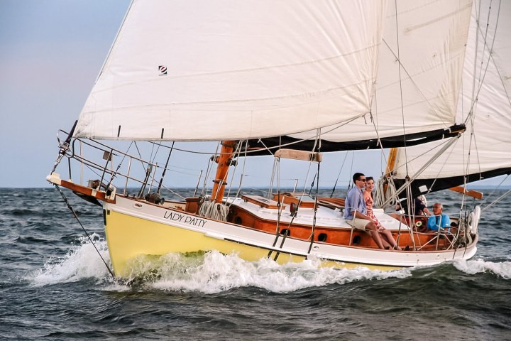 Sailboat 'Lady Patty' on water with three people aboard, sails full in the wind.
