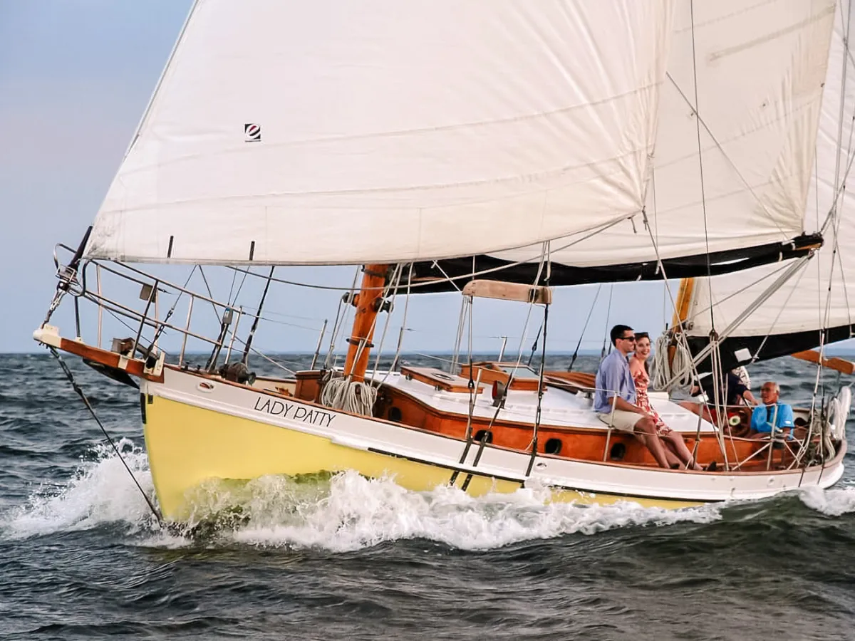 Sailboat 'Lady Patty' on water with three people aboard, sails full in the wind.
