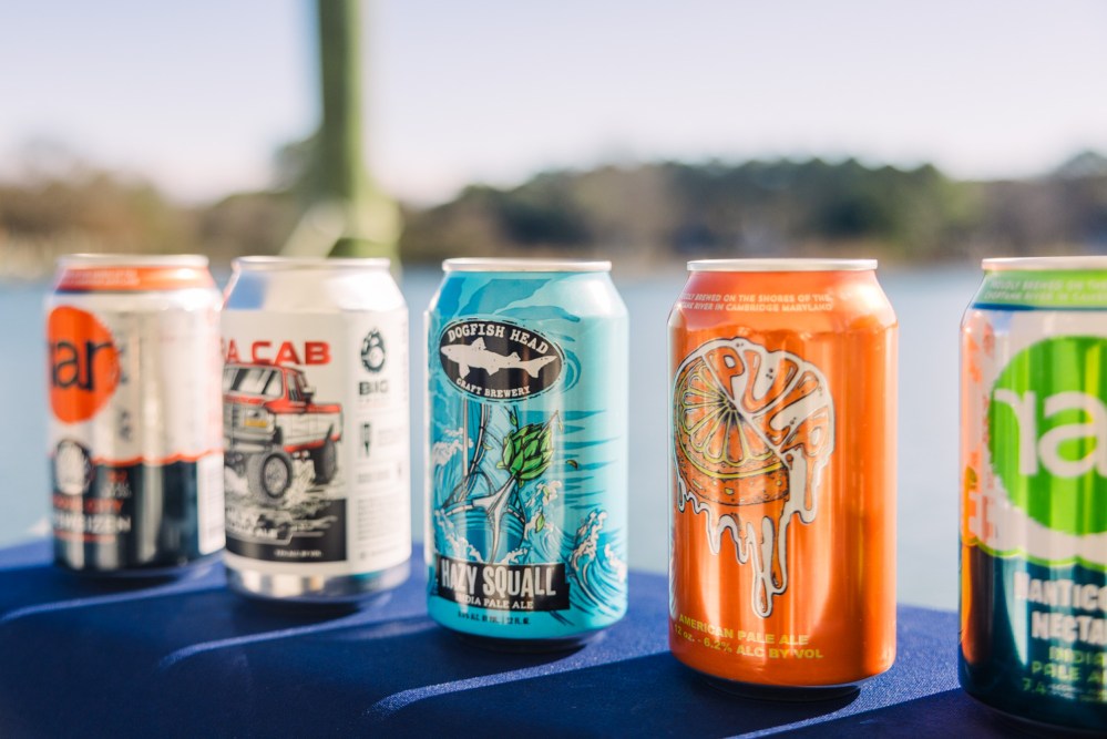 Five colorful beer cans on a blue table with blurred outdoor background.