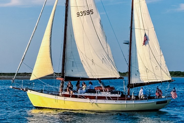 Yellow sailboat with two sails and people onboard on a sunny day.