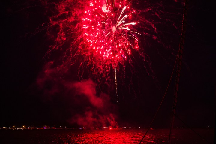 Bright red fireworks explode in night sky over water with reflections.