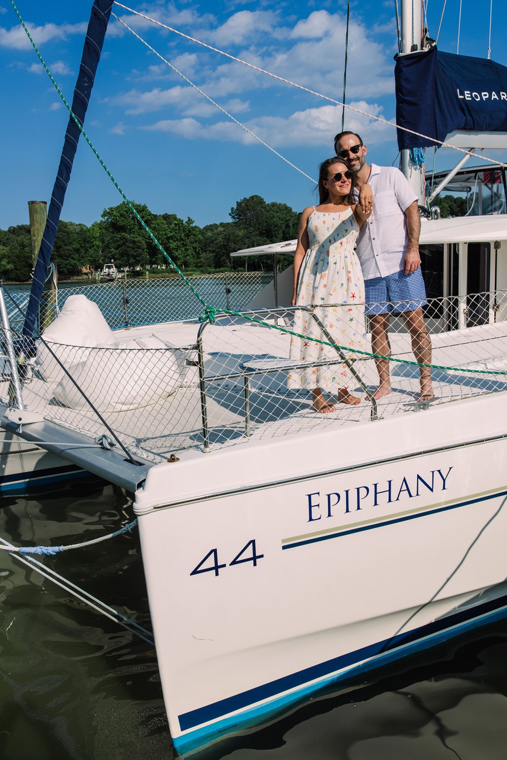 Man and woman smiling on a sailboat named Epiphany, under a blue sky.