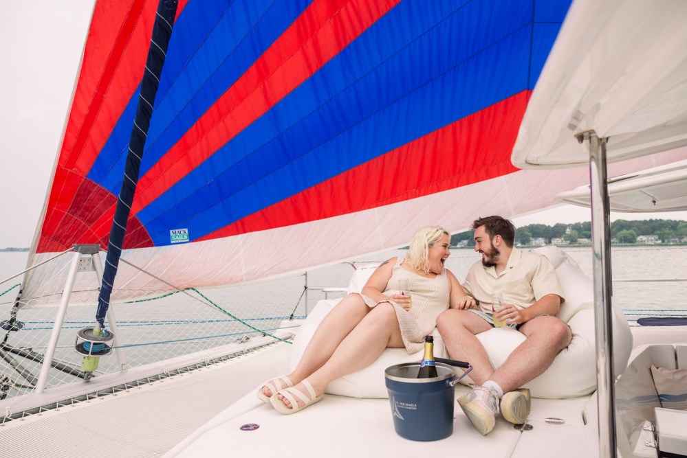 Smiling couple relaxing on a sailboat with colorful sail.