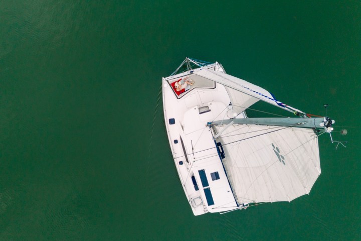 Aerial view of a white sailboat on a green sea.