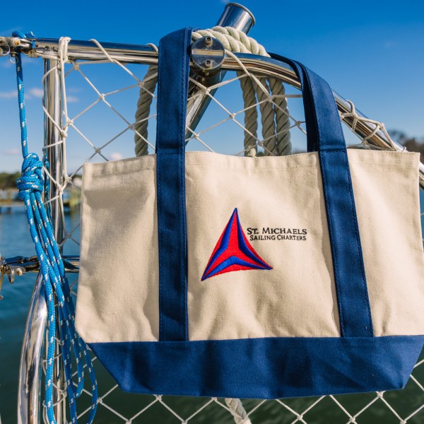 Canvas tote bag with blue straps hanging on a boat net, lake background.
