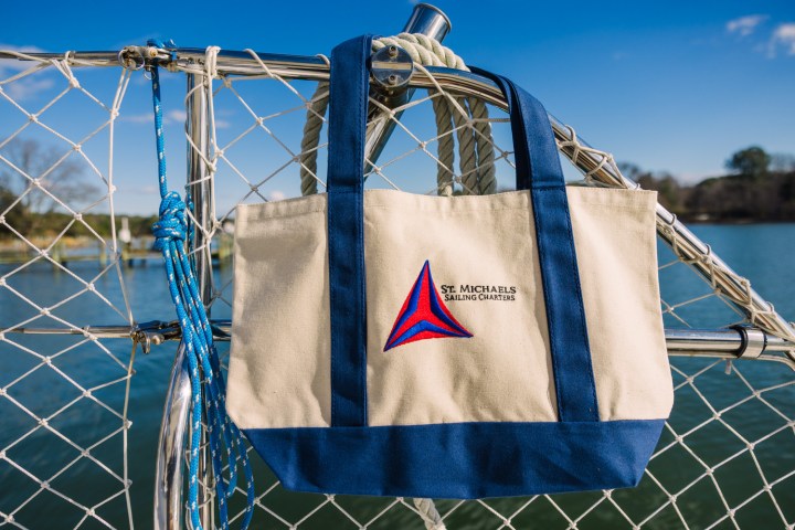 Canvas tote bag with blue straps hanging on a boat net, lake background.