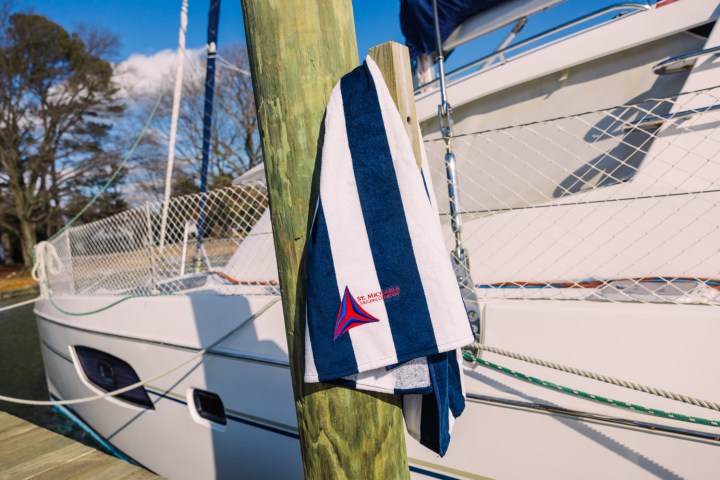 Striped towel hanging on a pole by a moored sailboat at a dock.