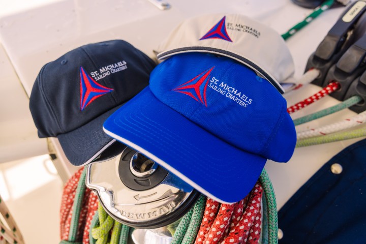 Three caps with sailing logos on a boat winch, surrounded by colorful ropes.