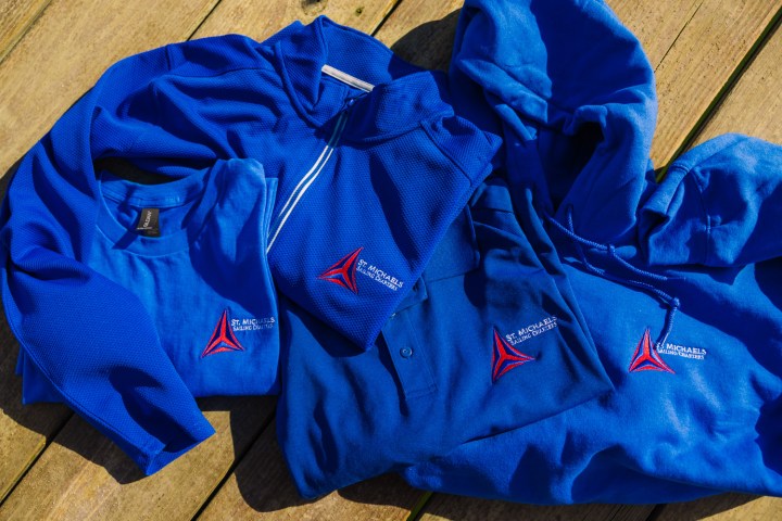 Blue apparel items with 'St. Michaels Sailing Charters' logo on wooden surface.