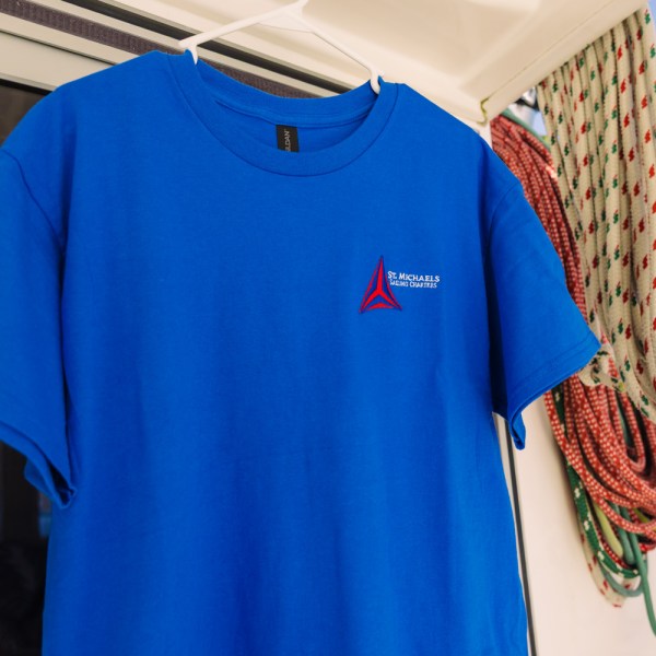 Blue T-shirt with logo hangs near coiled ropes on a boat.