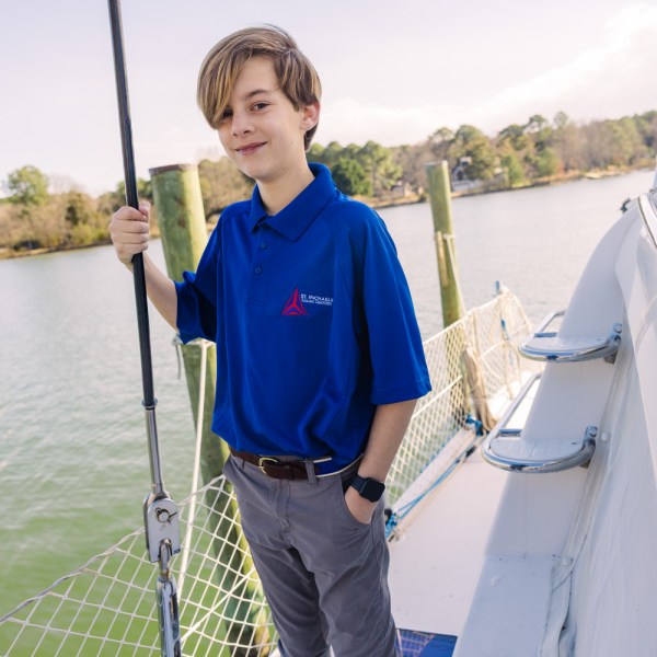 Young person in blue shirt standing on a boat by the water.