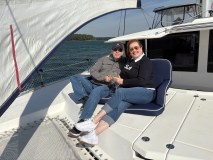 Couple smiling and relaxing on a boat with a drink and sail in the background.