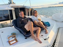 Smiling couple relaxing with drinks on a boat deck during sunset.