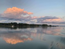 Lake at sunset with pink clouds and tree-lined shore.