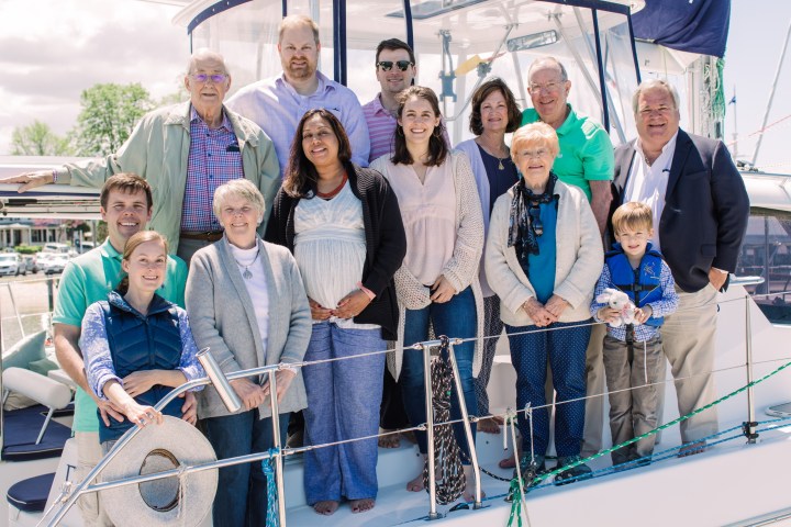 Group of thirteen people posing on a boat deck in casual attire on a sunny day.
