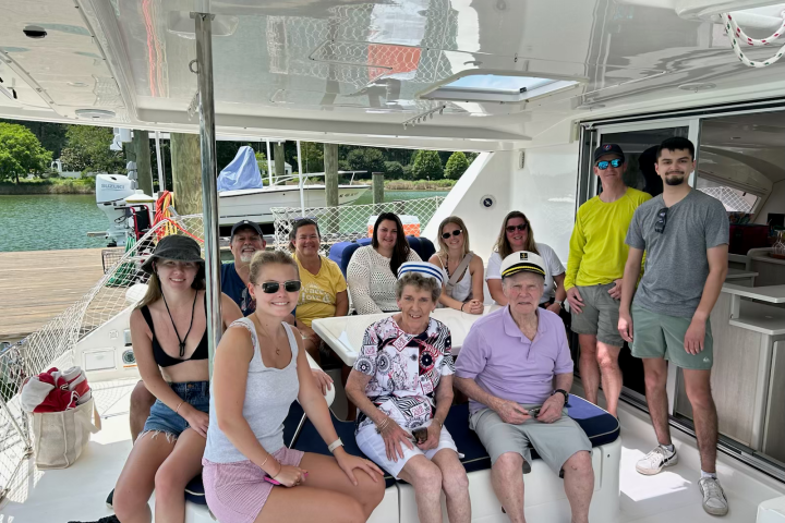 Group of people smiling on a boat by a waterfront on a sunny day.