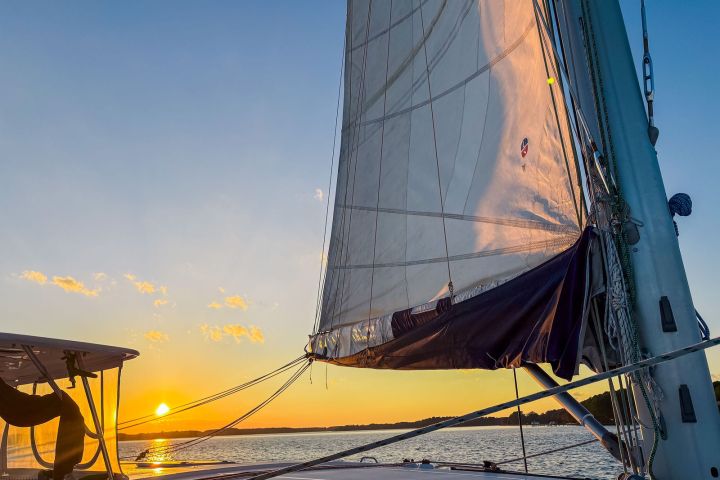 Sailboat on water at sunset, with sails catching the light and a clear sky.
