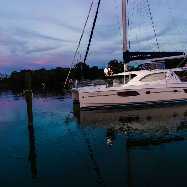 Sailboat moored on calm water at dusk, reflecting colorful clouds and sky.