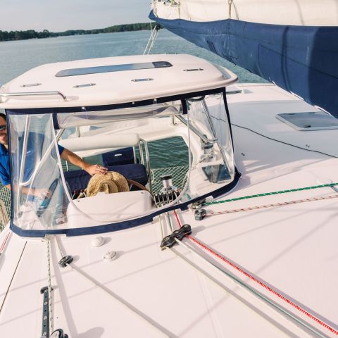 Person navigating a sailboat on a sunny day, near the shore.