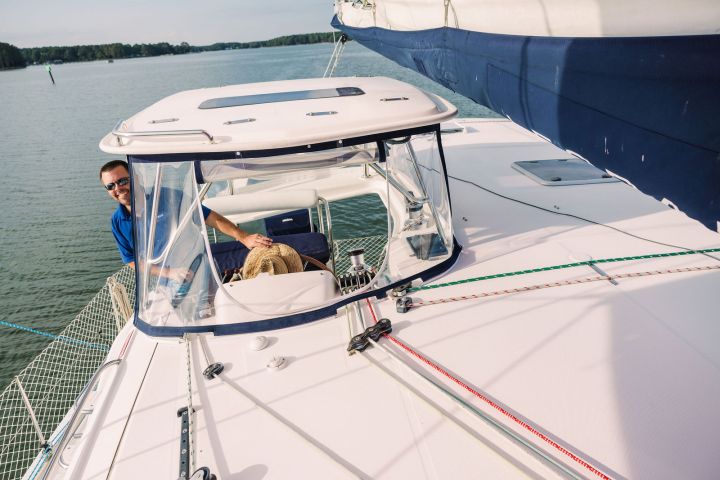 Person navigating a sailboat on a sunny day, near the shore.
